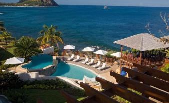 a resort with a pool surrounded by lounge chairs and umbrellas , overlooking the ocean at Cap Maison Resort & Spa