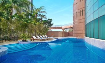 a large swimming pool with a red and white striped border is surrounded by lounge chairs and palm trees at Hilton Beirut Metropolitan Palace