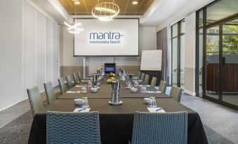 a conference room with a long table , chairs , and a screen displaying the mantra logo at Mantra Mooloolaba Beach