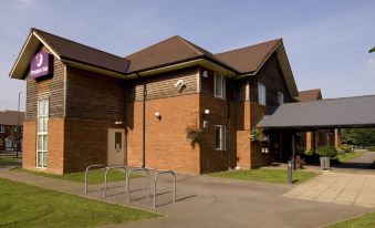 a brick building with a parking lot in front of it , surrounded by grass and trees at Premier Inn Tewkesbury