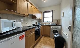 a kitchen with wooden cabinets and black appliances , a window , and a trash can next to a window at River View Apartment