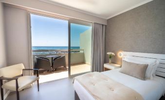a hotel room with a large bed and sliding glass doors leading to a balcony overlooking the ocean at Arribas Sintra Hotel