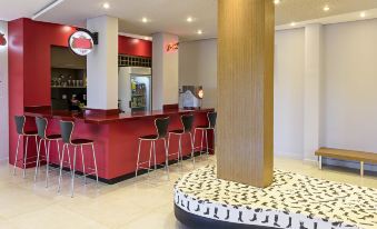 a modern lounge area with a red bar counter , white and black patterned floor mats , and several chairs at Ibis Styles Birigui