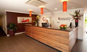 "a reception desk with a wooden finish and red pendant lights in the background , labeled "" vine country motor inn "" on the wall" at Wine Country Motor Inn