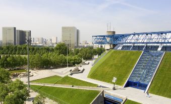a large blue building with a green roof , surrounded by grass and trees , and located in an urban area at Ibis Styles Paris Mairie de Montreuil