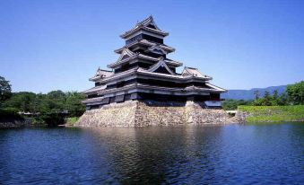 a large , ornate castle on a lake , surrounded by lush greenery and a clear blue sky at Ace Inn Matsumoto