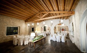 a large , well - lit room with wooden beams and white walls , filled with tables and chairs arranged for a formal event at Castello Camemi