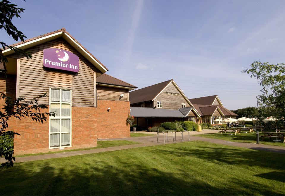 "a brick building with a purple sign that says "" premier inn "" is surrounded by a grassy yard" at Premier Inn Tewkesbury