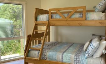 a wooden bunk bed with a ladder is in a room with a window and a rug at Driftwood Villas