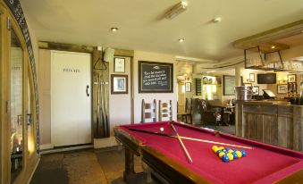 a pool table with a pink felt surface and balls is in a room with white walls at The Woolpack Inn