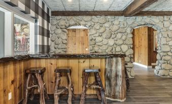 a rustic kitchen with stone walls , wooden floors , and three stools placed at the front of the counter at The Creekstone
