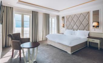 a luxurious hotel room with a large bed , white bedding , and a view of the ocean at Heritage Grand Perast by Rixos