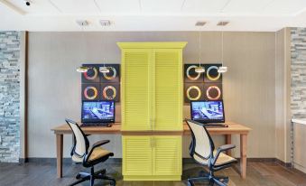 a yellow cabinet with two computer monitors on top and a black chair in front at Home2 Suites by Hilton Richmond Hill Savannah I 95