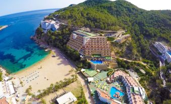 aerial view of a resort on a beach with multiple buildings and pools , surrounded by mountains at Hotel Galeón