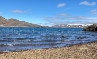 a serene lake surrounded by snow - covered mountains , with a rocky shoreline in the foreground at Motel Arctic Wind