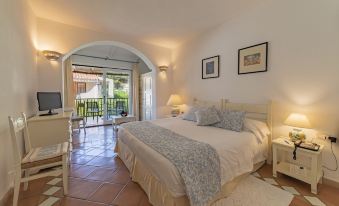 a bedroom with a large bed and white linens , next to an open door leading to a balcony at Club Hotel Baja Sardinia