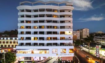 a tall white building with a curved design , situated next to a street with cars and pedestrians at Gold Crest Hotel