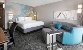 a modern hotel room with a white bed , blue accent chair , and a gray sofa at Courtyard by Marriott Las Vegas Convention Center