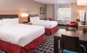 a hotel room with two beds , each bed having white linens and red skirt , along with a dining table and chairs at TownePlace Suites Merced