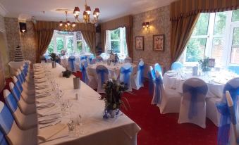 a long dining table is set with white tablecloths and blue chairs , surrounded by chairs and chandeliers at Woodlands Hotel