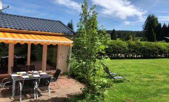 a small house surrounded by a lush green garden , with a dining table and chairs set up for a meal at Mimi