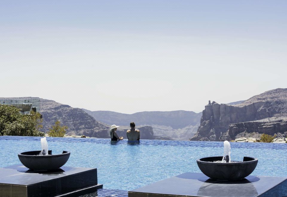 a man is swimming in a large infinity pool , surrounded by mountains and a clear blue sky at Anantara Al Jabal Al Akhdar Resort