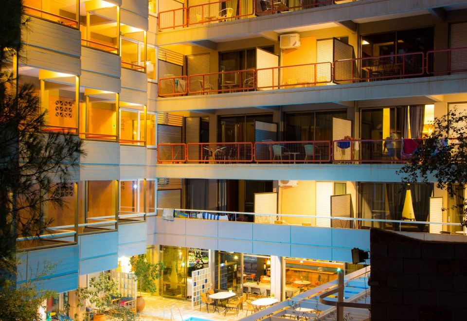 a nighttime view of an apartment building with a pool , surrounded by trees and lit up with orange lights at Apollonia Hotel Apartments