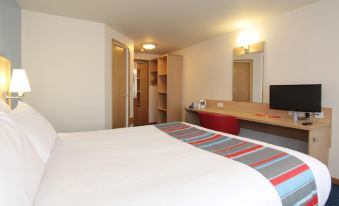a hotel room with a comfortable bed , a desk , and a television mounted on the wall at Travelodge St. Clears Carmarthen