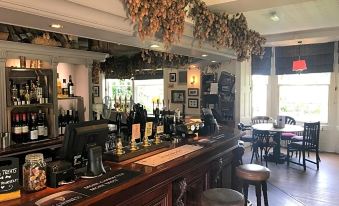 a well - decorated bar with wooden tables and chairs , along with various bottles and cups on the counter at The Mortimer Arms