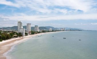 a beach scene with a few boats and buildings in the background , under a blue sky with clouds at Resort de Paskani