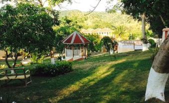 a lush green lawn with a gazebo in the background , surrounded by trees and bushes at Paradise Reggae Resort