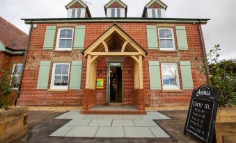 a red brick building with green shutters and a wooden porch , situated on a cobblestone street at Woodfalls Inn