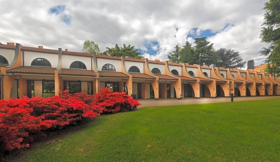 a large building with a red roof and arched windows is surrounded by a green lawn and red flowers at Hotel Pineta