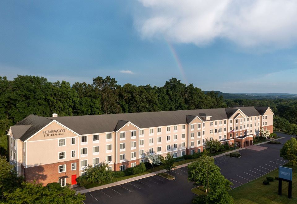 a large hotel with a green tree and white wall in the background , under a blue sky with a rainbow at Homewood Suites by Hilton Wallingford-Meriden
