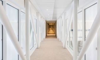 a long , white hallway with white walls and beige carpet , leading to an open space at the end at Best Western le Beffroi