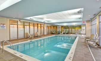 an indoor swimming pool with a large , empty space and white tiled floors , surrounded by lounge chairs and umbrellas at Home2 Suites by Hilton Dickson City Scranton