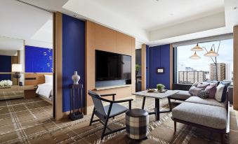 The living room is furnished with large windows, chairs, and a table in front of the TV at Hyatt Centric Kanazawa