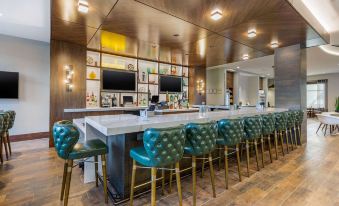 a modern bar area with a long white counter , multiple tvs , and several chairs arranged around it at Cambria Hotel - Arundel Mills BWI Airport