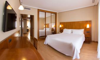 a hotel room with a large bed , white linens , and a wooden headboard , reflected in a mirror on the wall at NH San Pedro