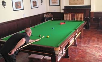 a man is playing pool in a room with a green pool table , surrounded by chairs and paintings on the walls at The Crown Hotel