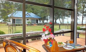 a wooden table with a vase of flowers sits in front of a window overlooking a grassy area and trees at HaadSon Resort