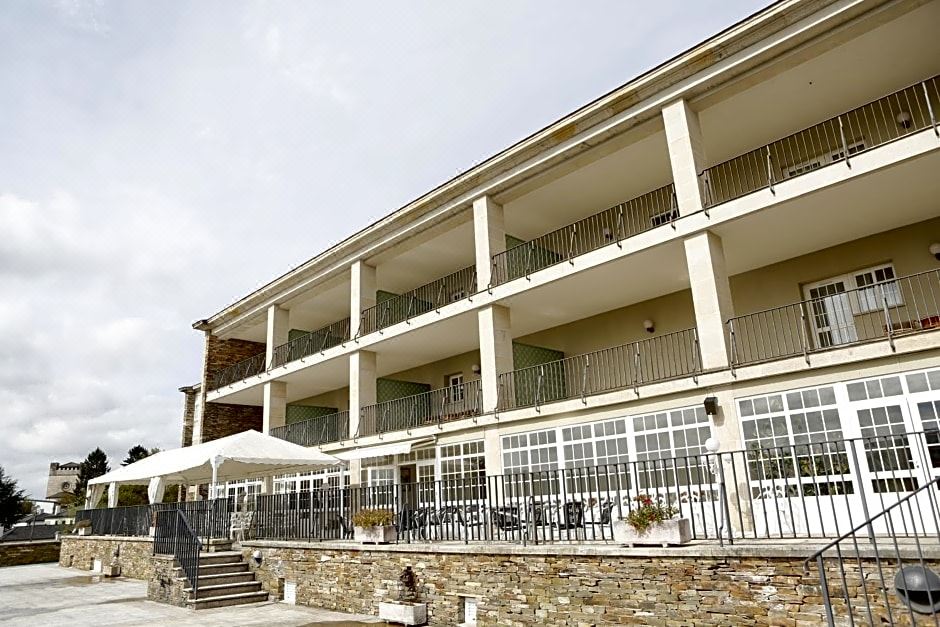 a large , modern building with multiple balconies and a covered walkway , surrounded by stone walls and a patio area at Pousada de Portomarin