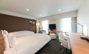 a modern hotel room with a large bed , white desk , and two chairs , all arranged in a minimalist style at Daiwa Roynet Hotel Numazu