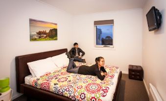 a woman is lying on a bed with a colorful blanket while another person sits on the same bed at The Island Accommodation