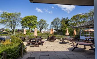 a courtyard with multiple picnic tables and umbrellas , creating a pleasant outdoor seating area for guests at Leeds / Bradford Airport