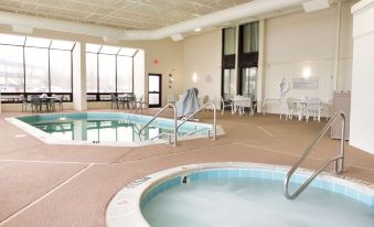 an indoor swimming pool with a jacuzzi , surrounded by chairs and tables , in a hotel lobby at Drury Inn & Suites St. Louis Airport