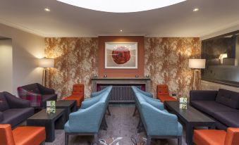 a modern living room with blue and orange chairs , a fireplace , and floral wallpaper on the walls at Castle Green Hotel in Kendal, BW Premier Collection