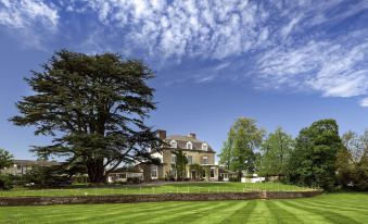 a large , stone house surrounded by lush green grass and trees , with a blue sky overhead at Mercure Bristol North the Grange Hotel