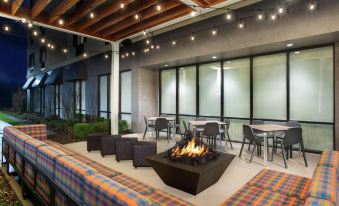 an outdoor seating area with a fire pit and seating , surrounded by tables and chairs at Home2 Suites by Hilton Long Island Brookhaven