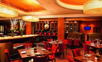 a dining room with red chairs and tables , a piano in the background , and a television mounted on the wall at The Ritz-Carlton, Marina del Rey